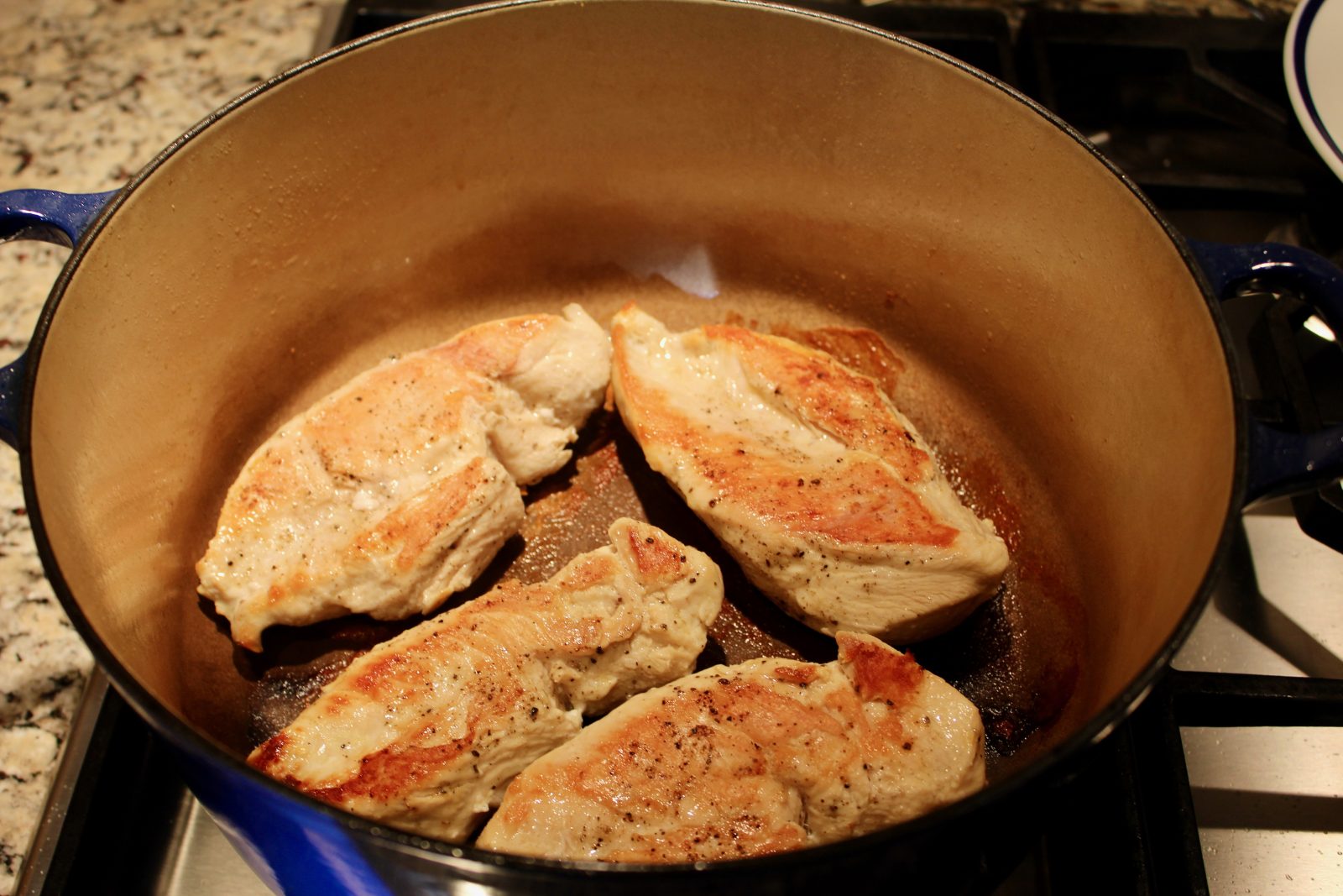 Recipe photo for White Chicken Chili showing a blue LeCreuset dutch oven with browned boneless skinless chicken breasts inside on gas stovetop.