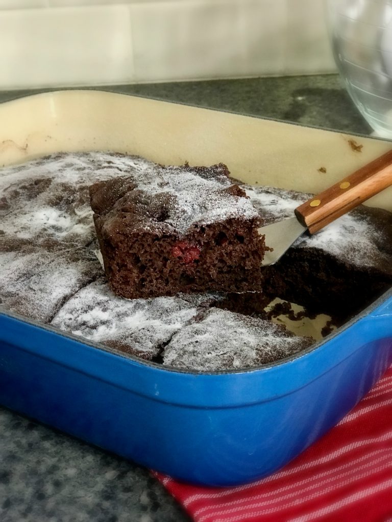 Chocolate Cherry Sheet cake in a 13 x 9 x 2-inch pan with piece cut out and dusted with powdered sugar