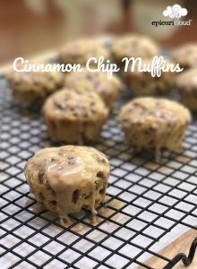 Cinnamon Chip Muffins drizzled with cinnamon glaze and cooling on black cooking rack place over parchment.