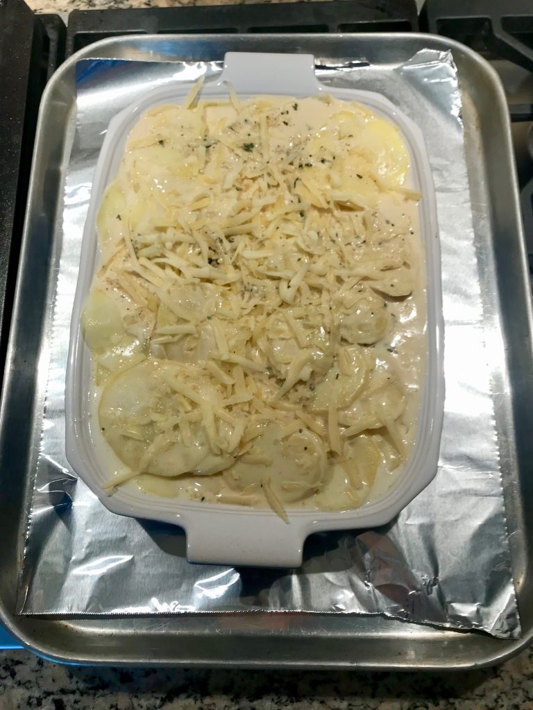 Casserole of Creamy Potatoes Au Gratin in rectangular stoneware baker placed on a foil line baking sheet, ready for baking.