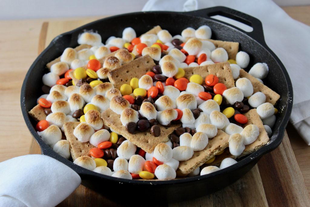 10" cast iron skillet filled with graham crackers, chocolate chips, reeses pieces candies and mini marshmallows just taken out of the oven. The chocolate chips are melty and the marshmallows are toasted