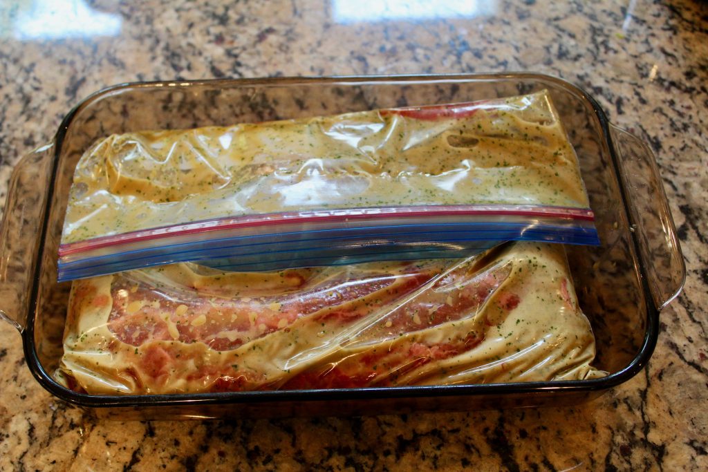 Flat iron steaks marinating in zip top bag placed in rectangular pyrex baking dish.