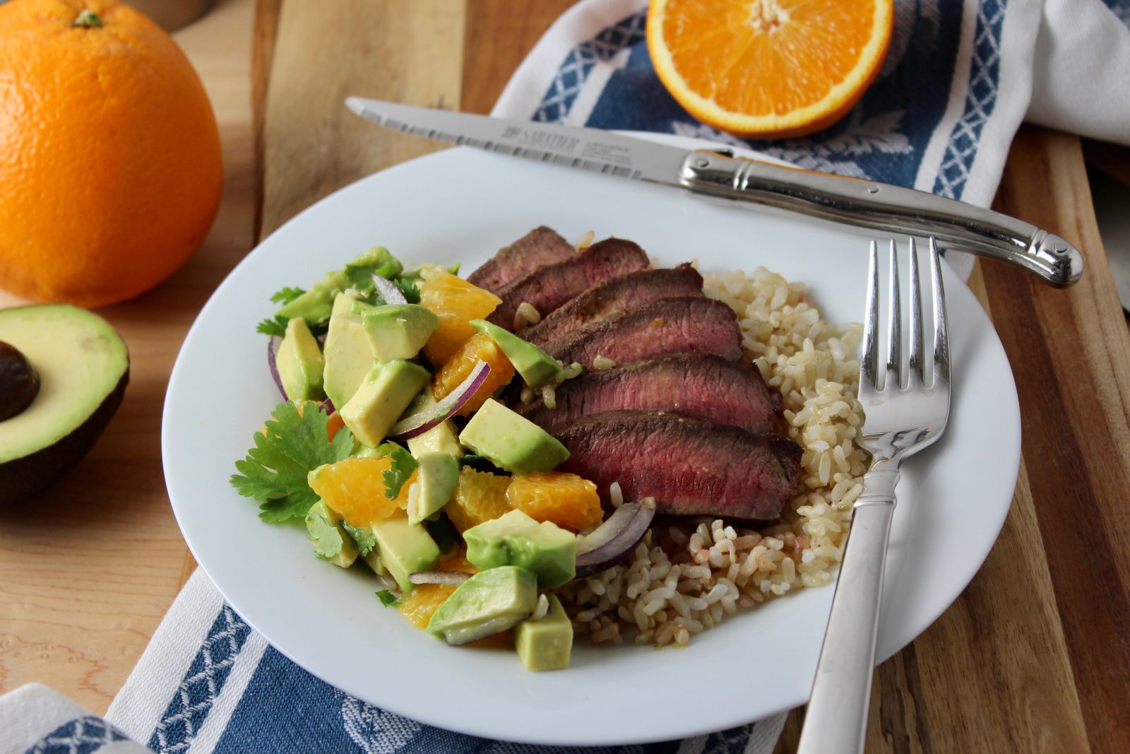 white round plate with brown rice, topped with fanned out grilled flat iron steak grilled medium with orange avocado salsa to the side.