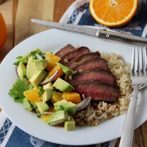 white round plate with brown rice, topped with fanned out grilled flat iron steak grilled medium with orange avocado salsa to the side.