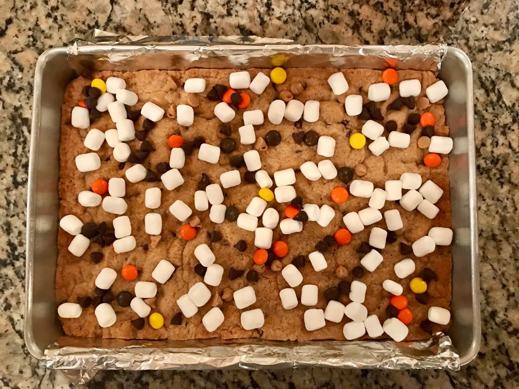 Peanut Butter S'mores Cookie Bars - 9x13x2-inch aluminum pan fitted with foil sling with baked dough being topped with marshmallows
