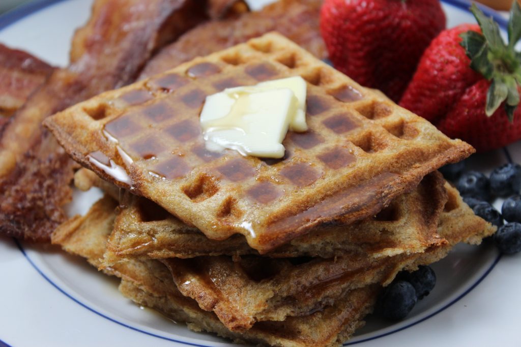 Yeasted Waffles: Close up photo of stacked square waffles with some pats of butter in the center and syrup dripping off the edges.