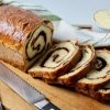 Homemade Cinnamon Swirl Bread with raisins with 4 sliced cut and shingled on cutting board, knife and green striped kitchen towel