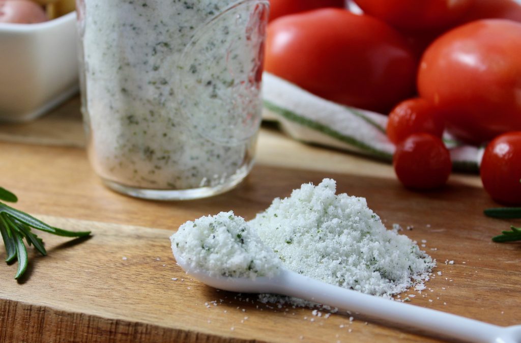 Homemade Rosemary Salt in mason jar.  close up view of rosemary salt on cutting board with vegetables in background