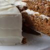 Recipe Photo for Cream Cheese Frosting Showing a 2 layer carrot cake frosted with cream cheese frosting on a white pedestal with a piece being lifted.