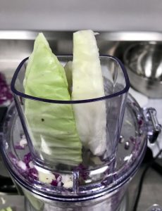 Two pieces green cabbage inserted into feed tube of food processor