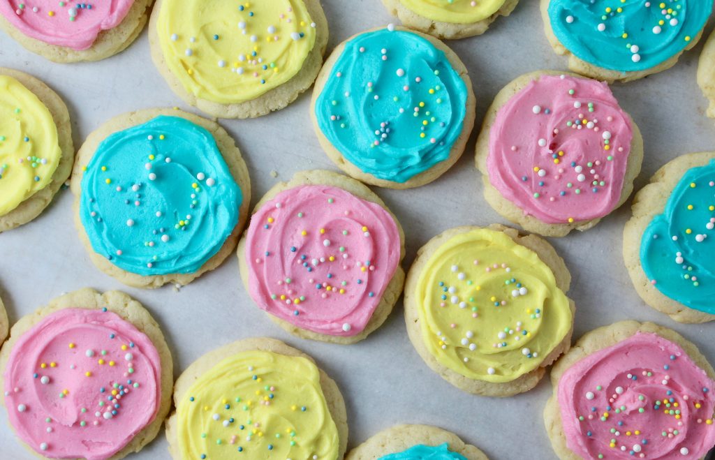 Cream Cheese Sugar cookies frosted in light pink, yellow and blue with nonpareil sprinkles - overhead shot of cookies on parchment 