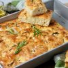 Focaccia bread in 13 x 9 x 2 metal pan topped with rosemary and coarse salt, slices cut and stacked