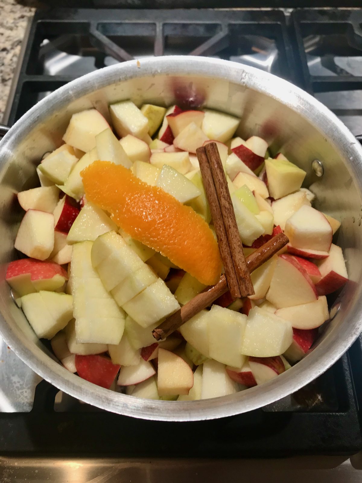 ingredients for applesauce in pot - chopped apples, cinnamon sticks, orange peel