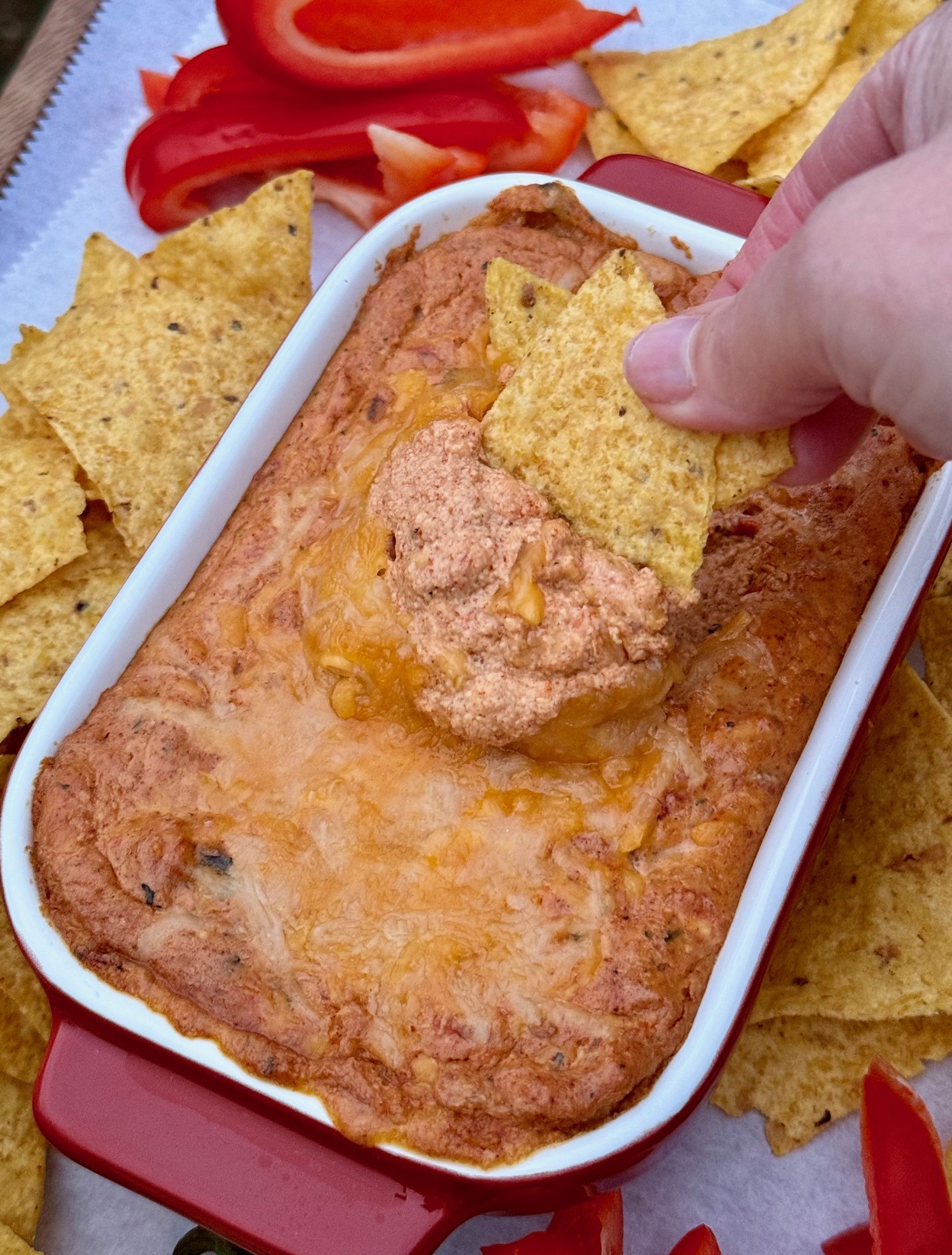 Rectangular dip with hot cottage cheese queso dip surrounded by tortilla chips and red bell pepper strips