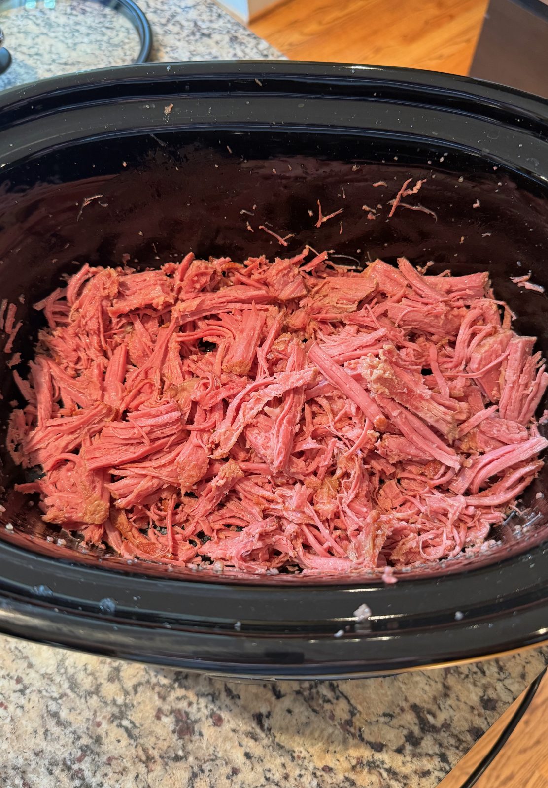 KitchenAid slow cooker with black insert on a granite countertop with shredded cooked corned beef preparing to make Slow Cooker Reuben Dip