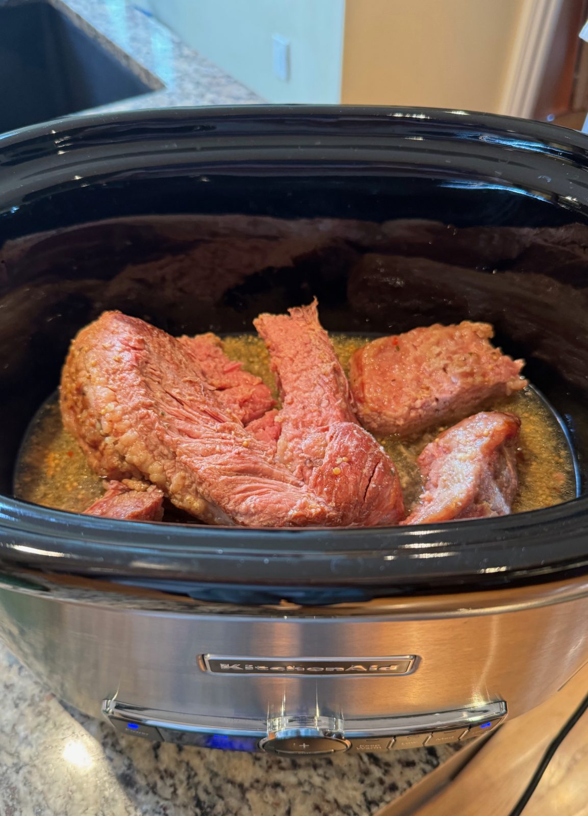 KitchenAid Slow Cooker on a a granite kitchen countertop with pieces of cooked corned beef in braising liquid.  Getting ready to make Slow Cooker Reuben Dip
