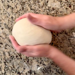 2 hands shaping some sourdough dough on a granite countertop