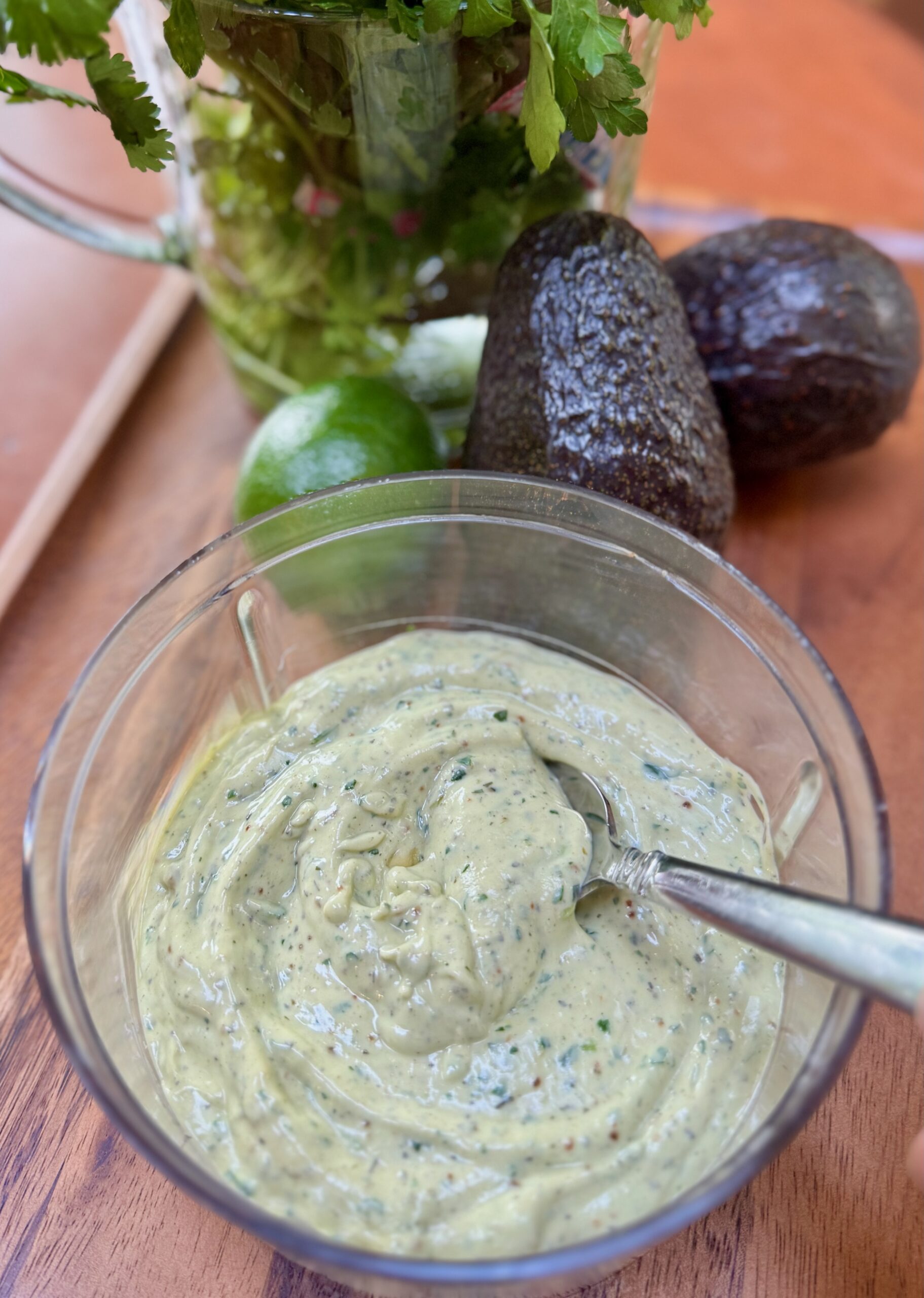 Pureed Avocado Ranch sauce in bowl from KitchenAid Top Down Cordless Chopper with avocado, lime and cilantro in the background.  All are seated on a wooden tray.