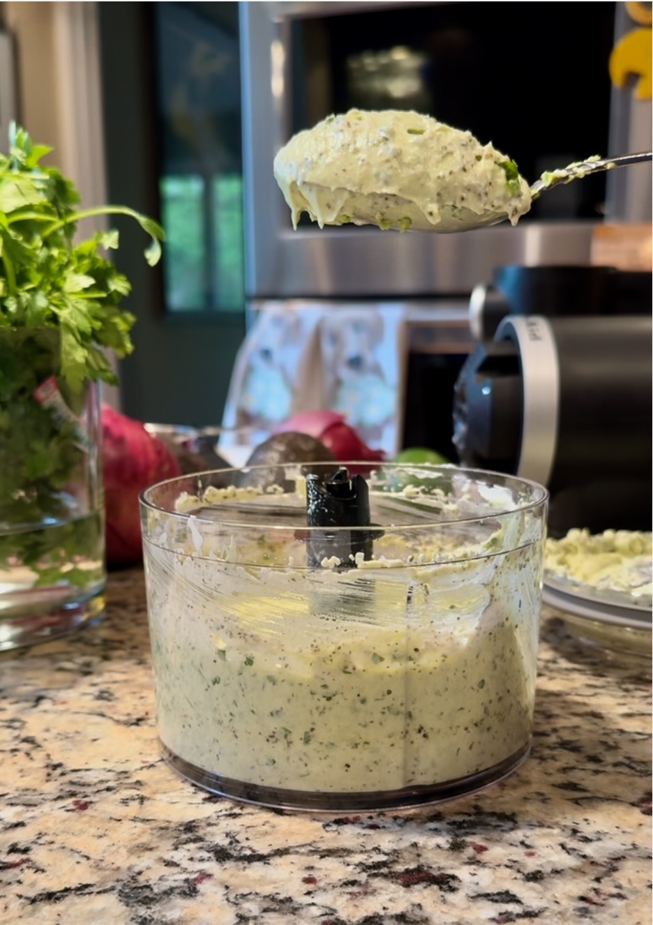 image of spoonful of pureed avocado ranch sauce.  In the bowl of the KitchenAid Top Down Chopper.