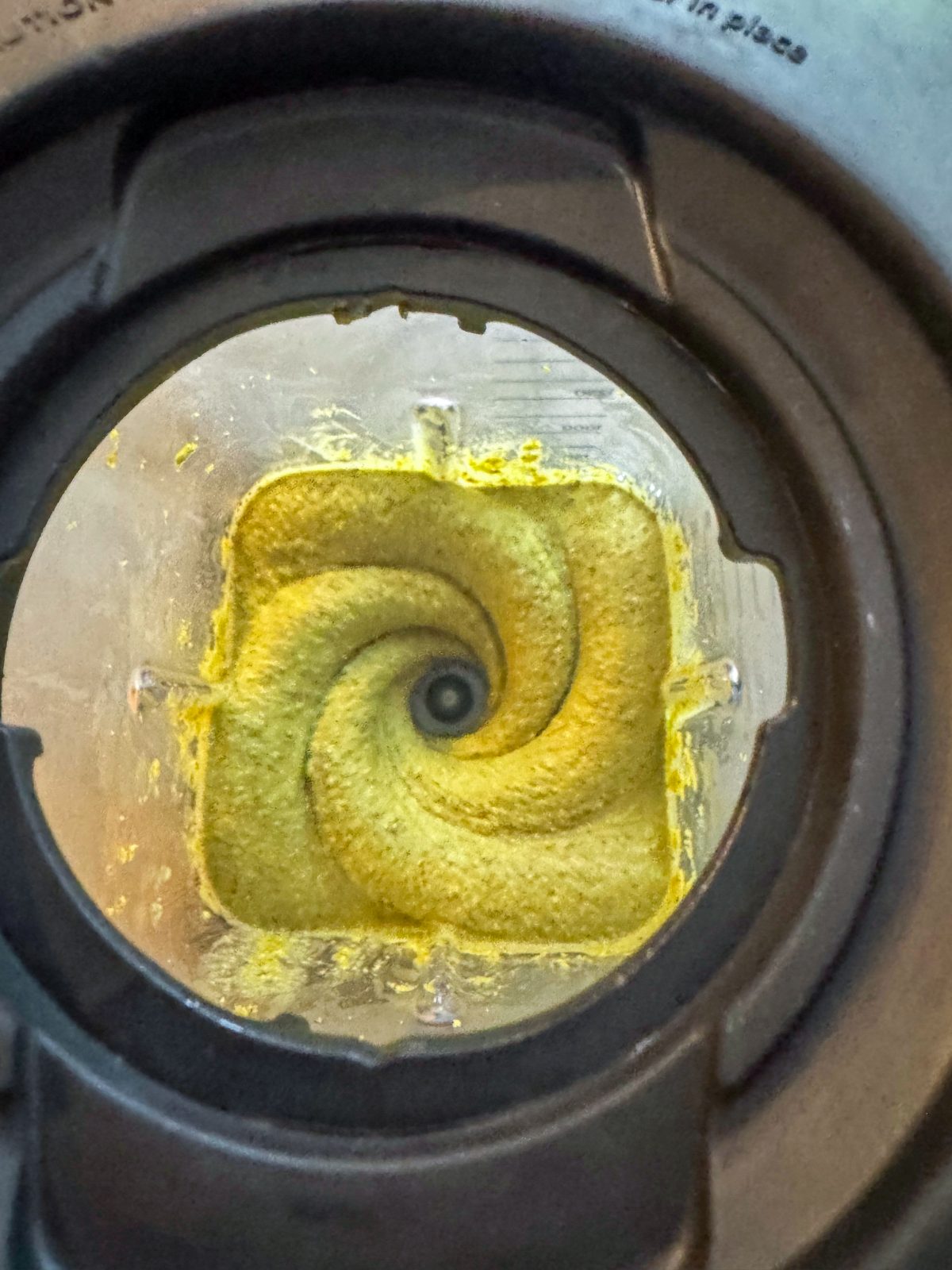 Pistachio butter churning in a blender through the black lid of the blender. beautiful swirl of thick green pistachio butter