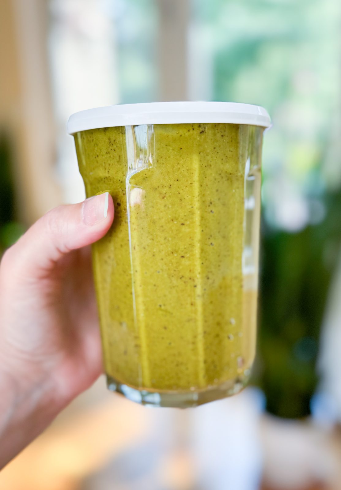 hand holding 16 ounce glass jar with white plastic lid filled with pistachio butter