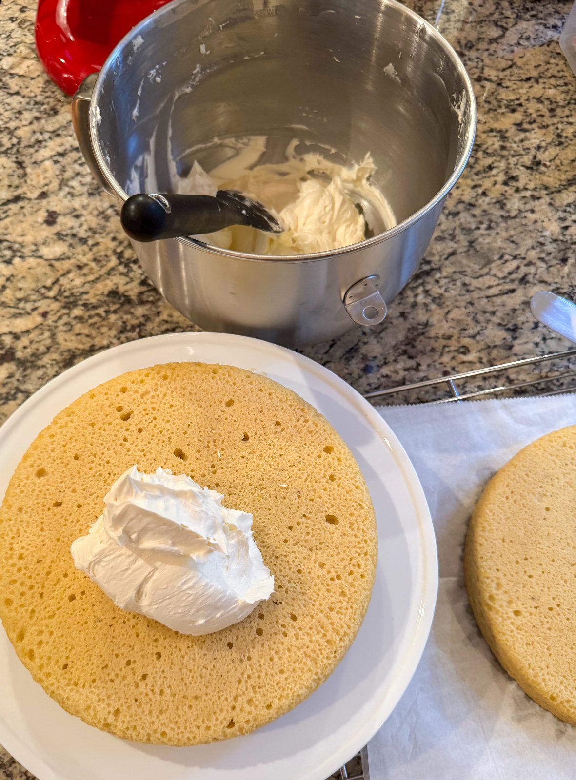 Recipe Photo for Less Sweet American Buttercream Frosting.  Whipped frosting in stainless steel stand mixer bowl.  Scoop of frosting on naked cake layer ready to be frosted.