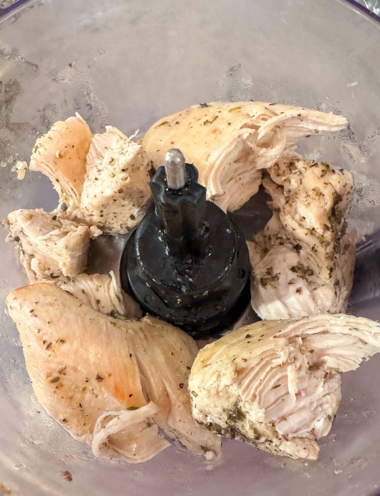 Seasoned and cooked chicken breast torn into large chunks in KitchenAid 7-cup Food Processor - preparing to be shredded