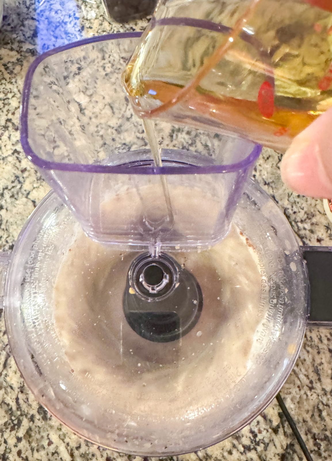 Olive oil being drizzled into running food processor making creamy honey mustard dressing