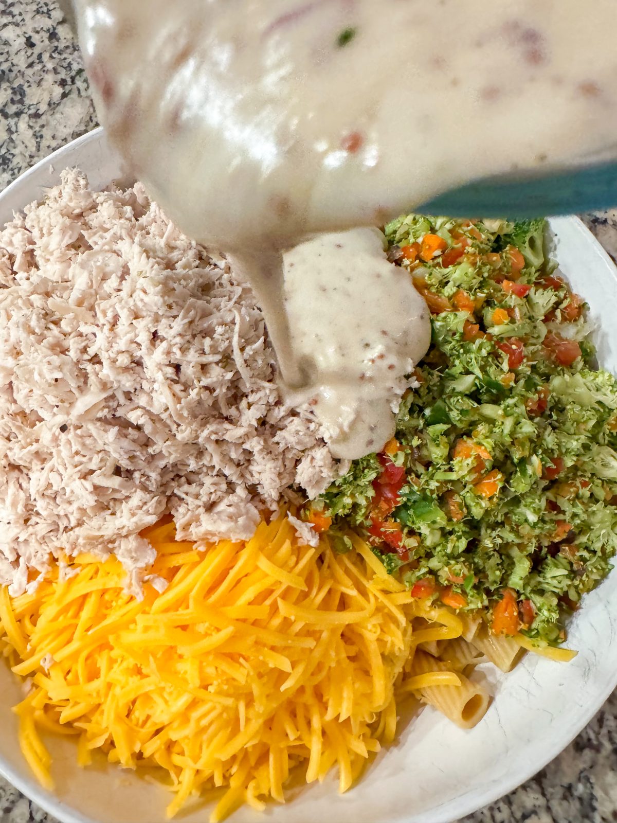 Recipe image for creamy honey mustard pasta salad. Overhead shot of rigatoni, chopped broccoli and red pepper, shredded cheddar cheese in a creamy honey mustard greek yogurt dressing.