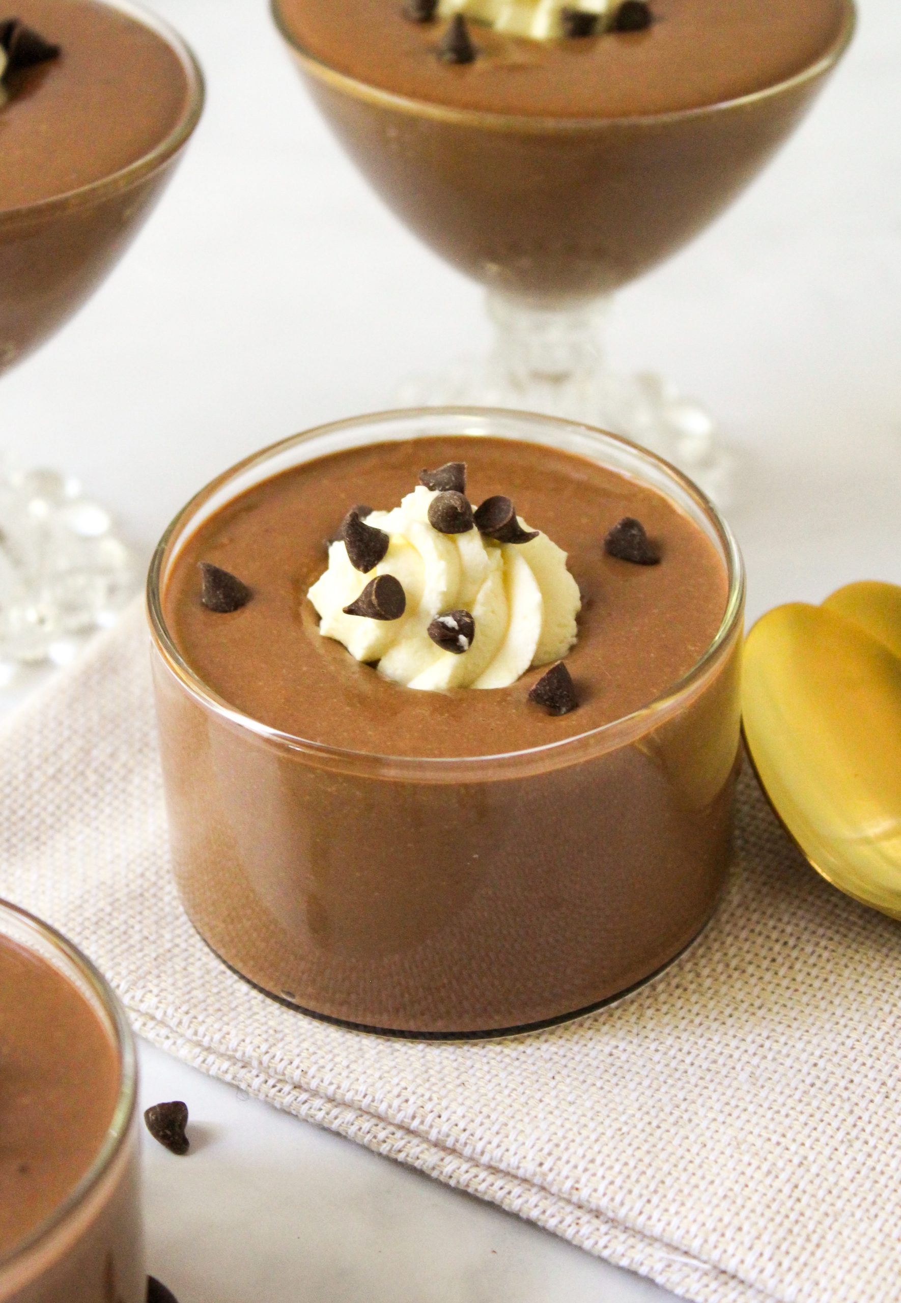 Finished Recipe Image of Cottage cheese chocolate pudding. pudding in a small straight sided glass dish with a dollop of whipped cream, mini chocolate chips and a gold spoon.