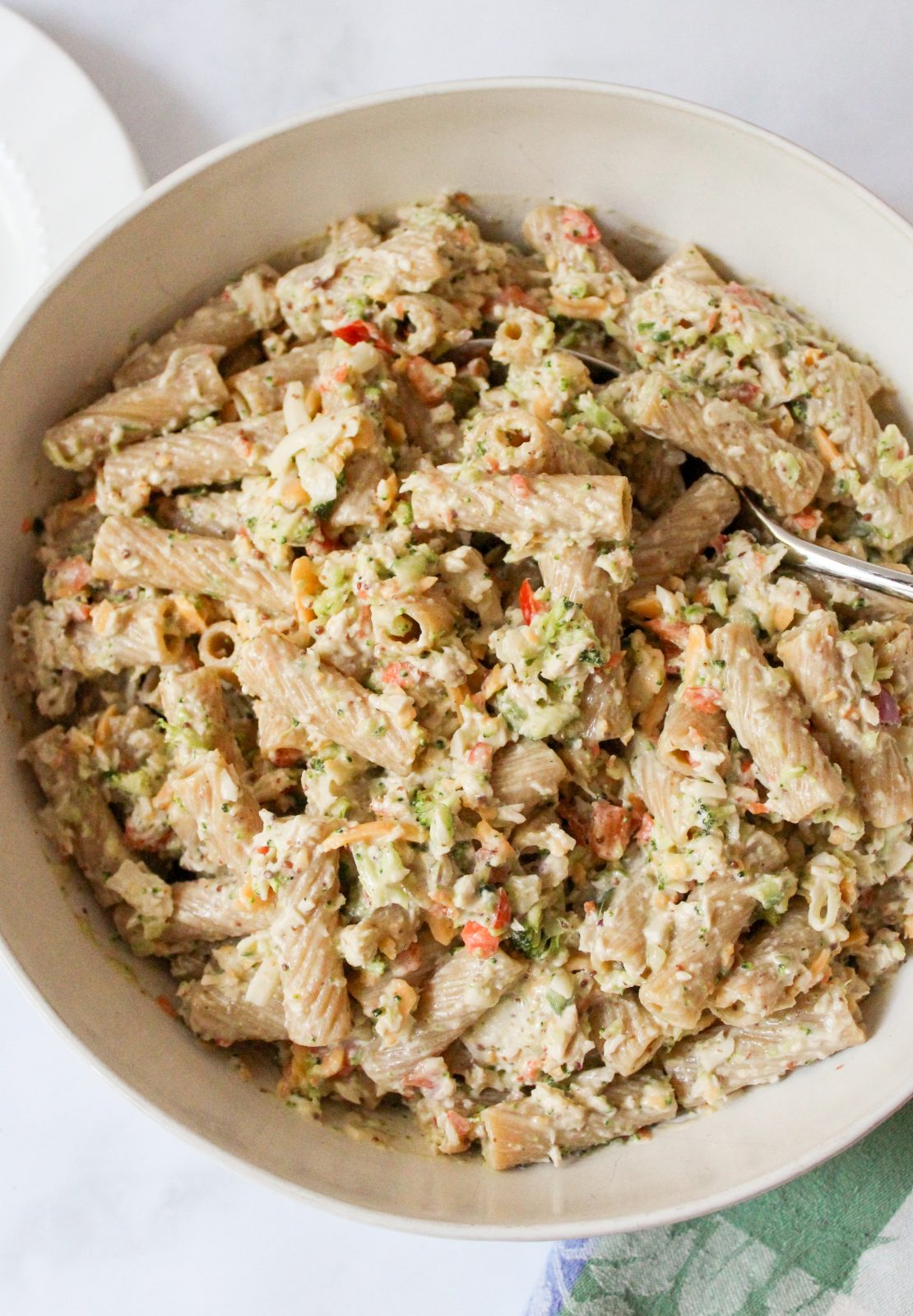 recipe image for creamy honey mustard pasta salad. Overhead shot of rigatoni, chopped broccoli and red pepper, shredded cheddar cheese in a creamy honey mustard greek yogurt dressing.