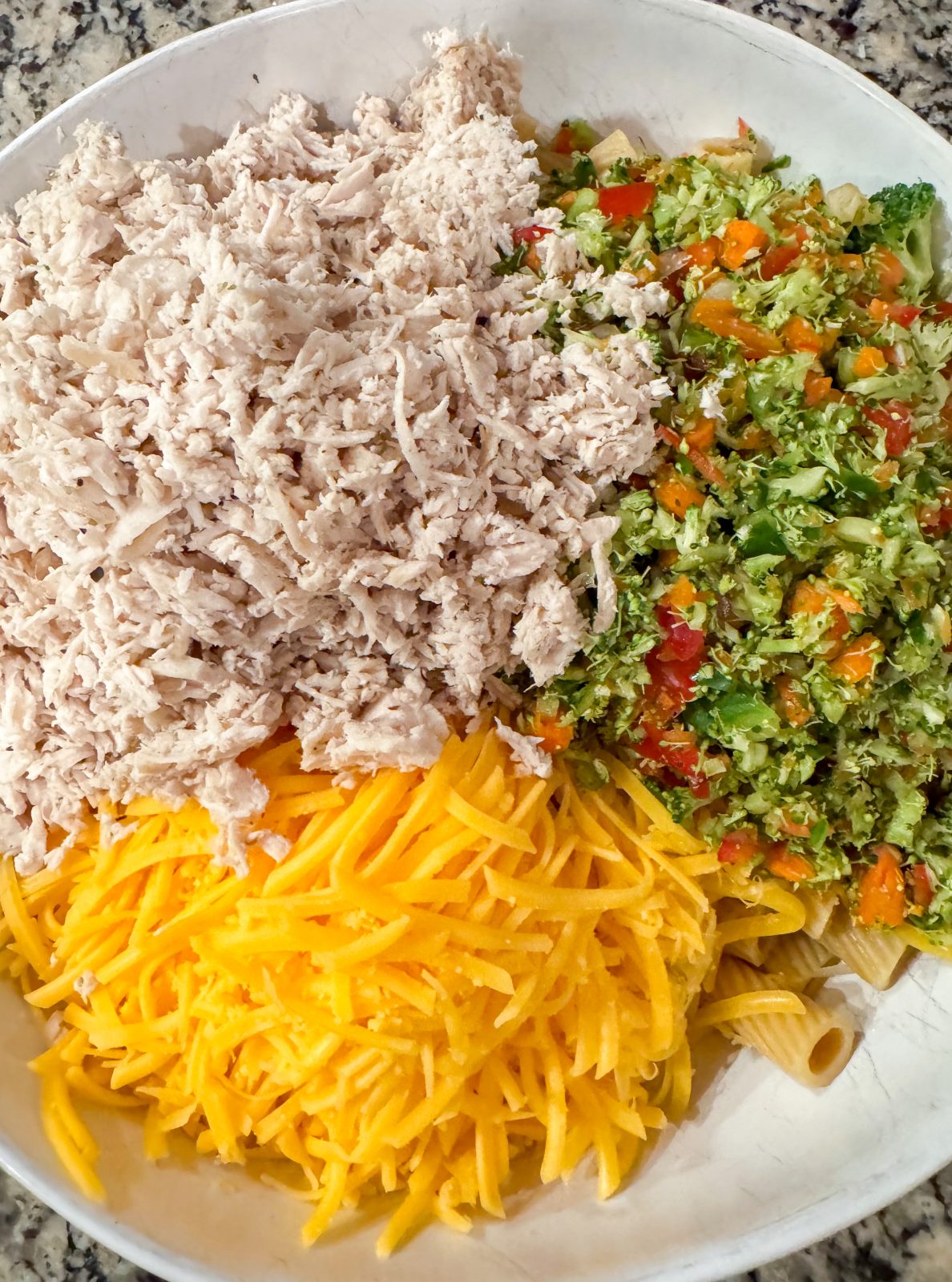 Recipe image for creamy honey mustard pasta salad. Overhead shot of rigatoni, chopped broccoli and red pepper, shredded cheddar cheese