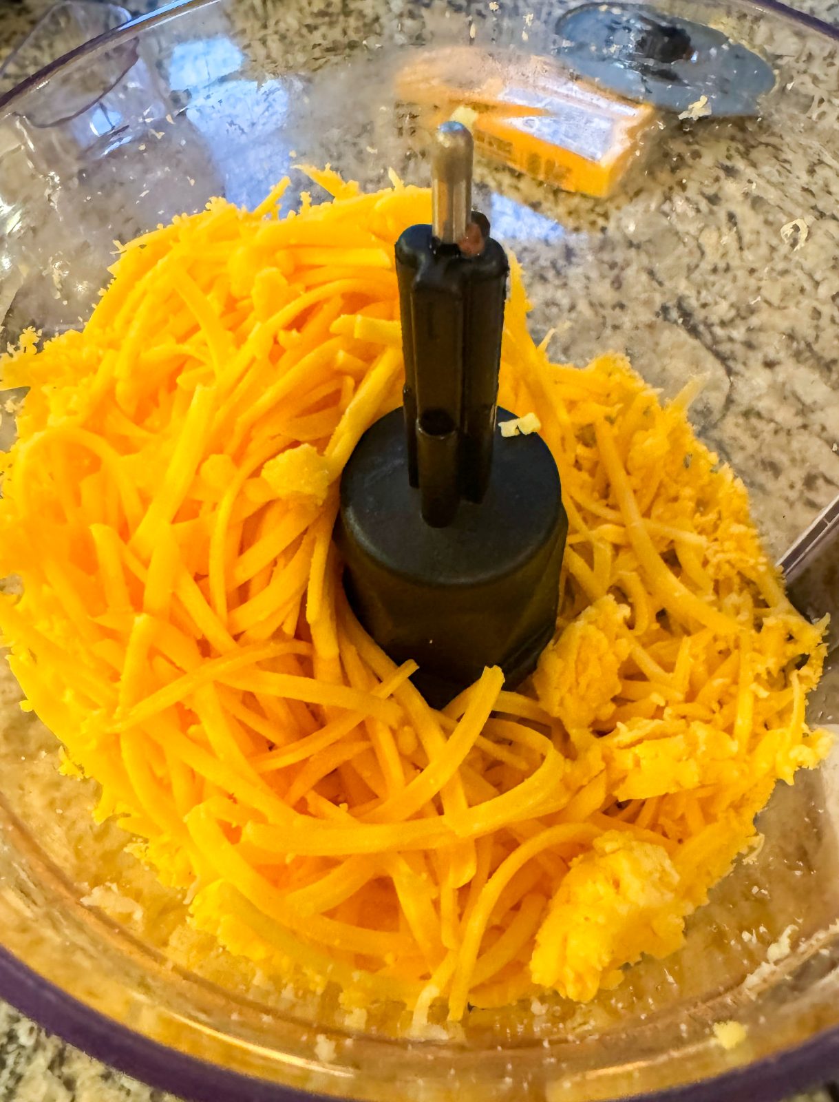 Yellow cheddar cheese shredded and in bowl of KitchenAid 7-cup Food Processor