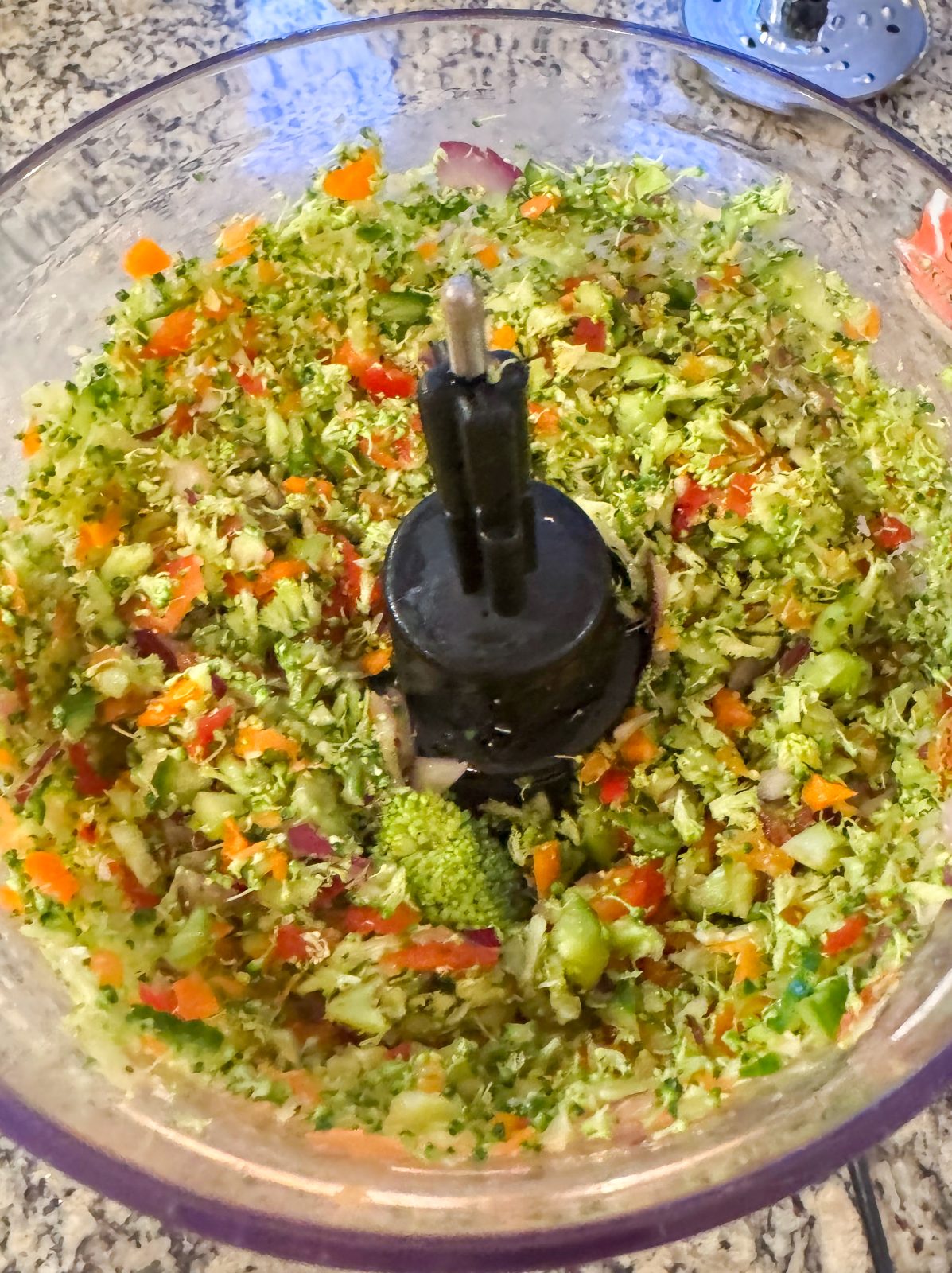 Chopped broccoli, cucumber, red bell pepper, red onion and carrot in a KitchenAid 7-cup food processor