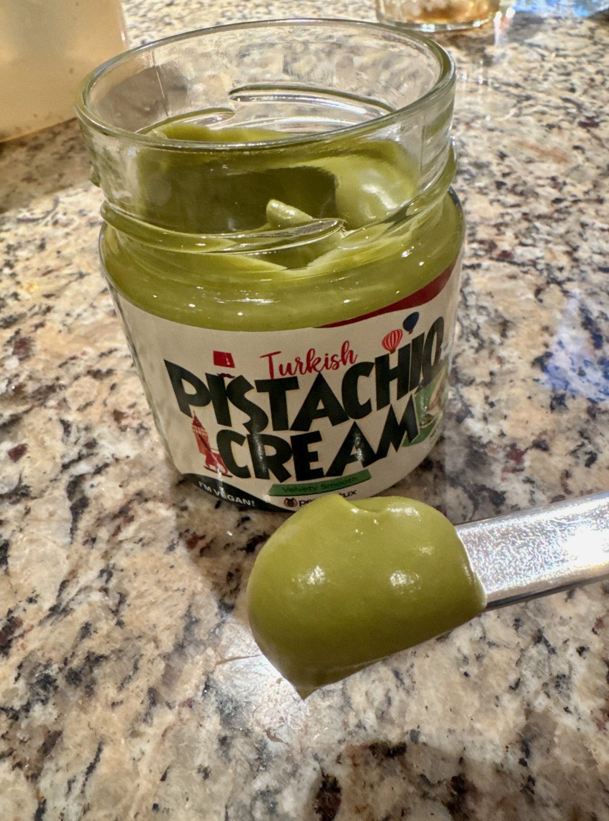Jar of Turkish Pistachio Cream. With lid off, spoon showing the smooth bright green cream.
