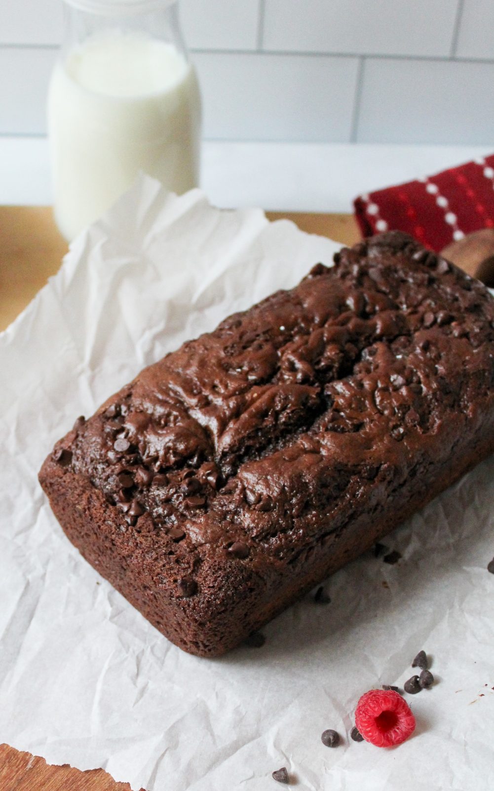 Recipe Photo for Easy Chocolate Loaf Cake. 45 degree angle landscape shot of chocolate loaf cake on parchment paper atop a wooden cutting board.
