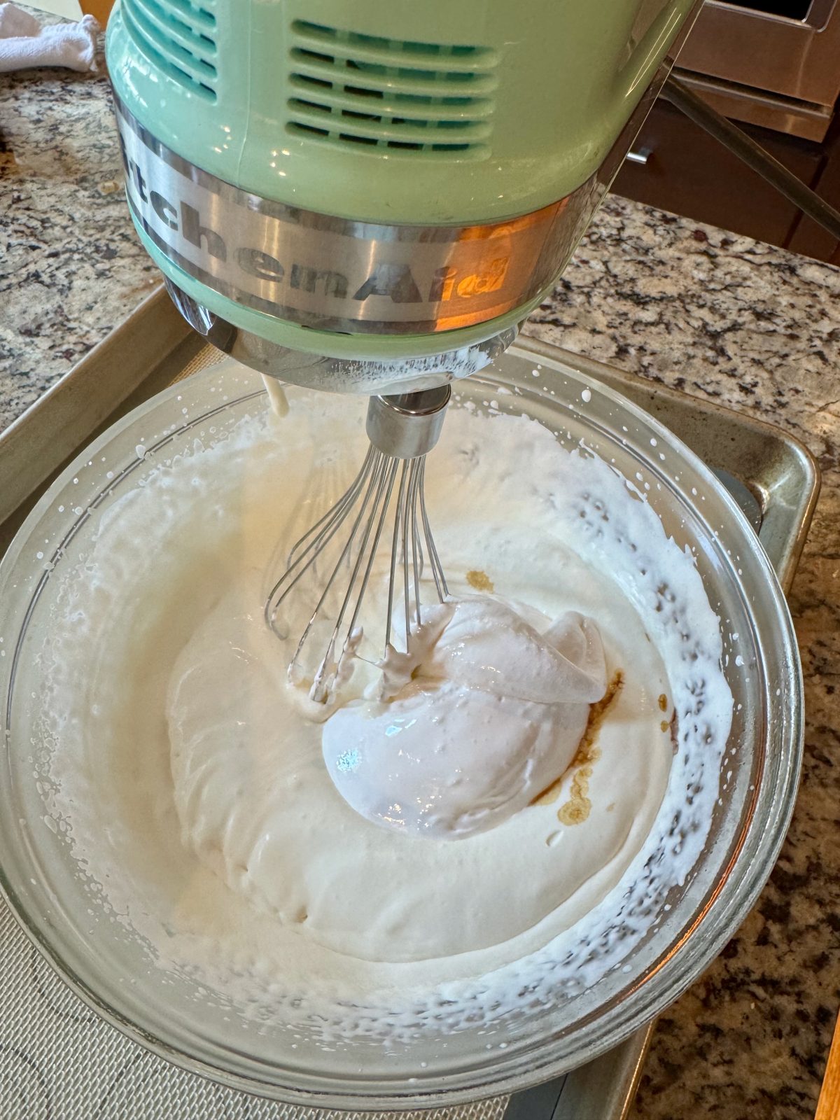 Recipe Photo for Frozen Marshmallow Whipped Cream Cocoa Toppers. Portrait orientation photo shows an Ice Blue KitchenAid Hand Mixer in with a Whisk beater attached whipping cream and vanilla and marshmallow fluff in a chilled glass bowl.