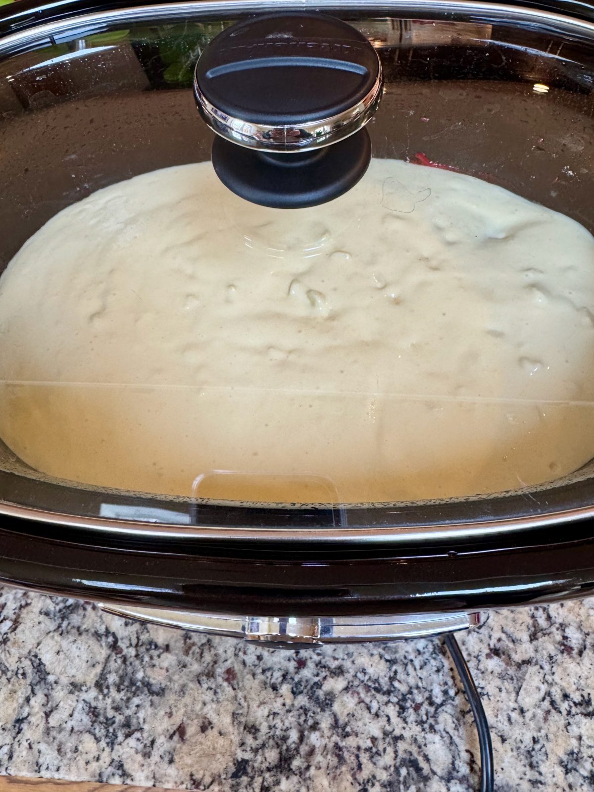Recipe Photo for Red Velvet White Chocolate (Slow Cooker) Lava Cake. A slow cooker contains the uncooked components of the cake.  You can see the white cream cheese mixture atop the red velvet cake mix.  The glass lid is covering the show cooker.