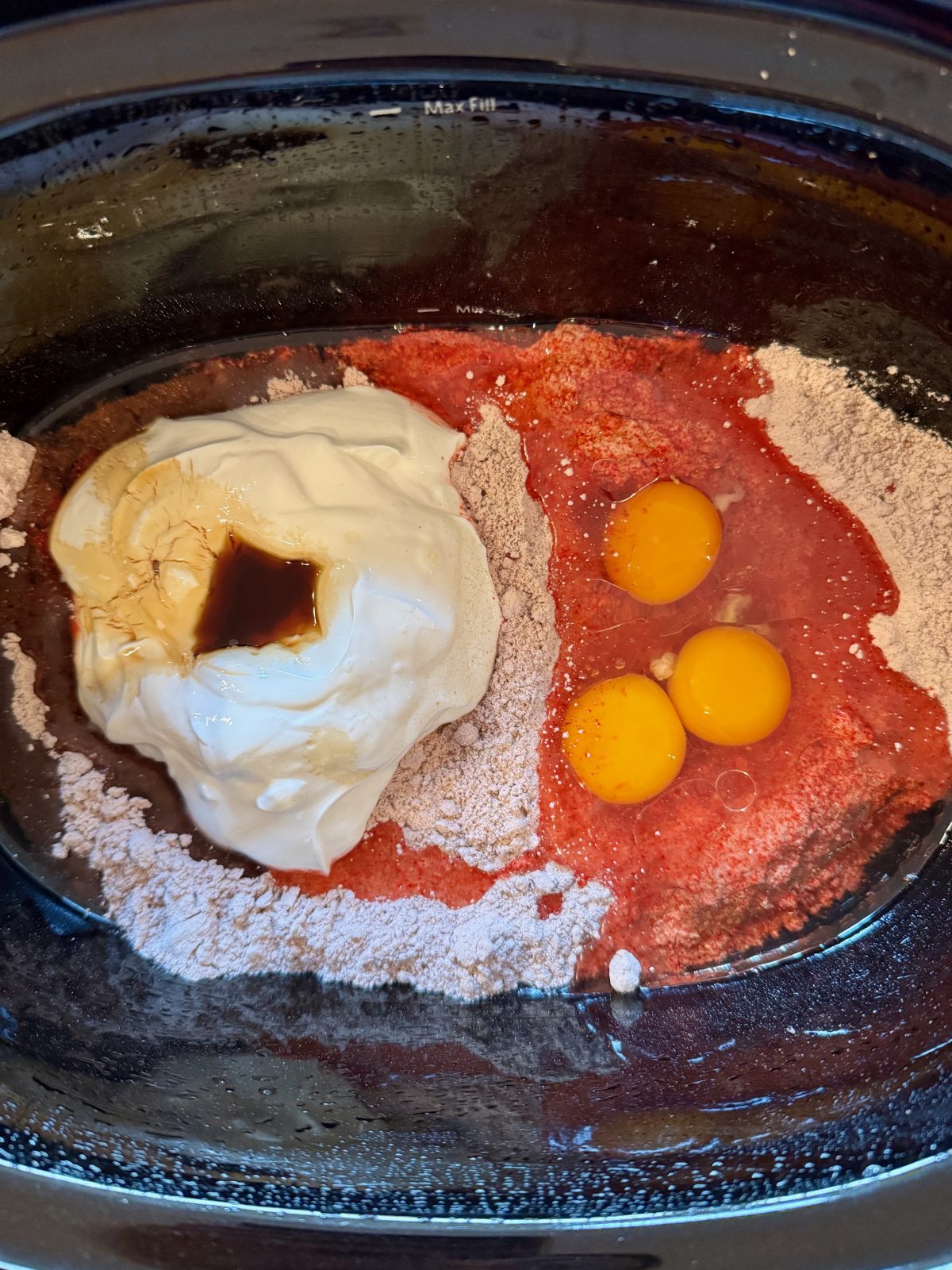 Recipe Photo for Red Velvet White Chocolate (Slow Cooker) Lava Cake.  the cake mix ingredients are gathered in the black slow cooker: red velvet cake mix, 3 eggs, oil, sour cream and vanilla.