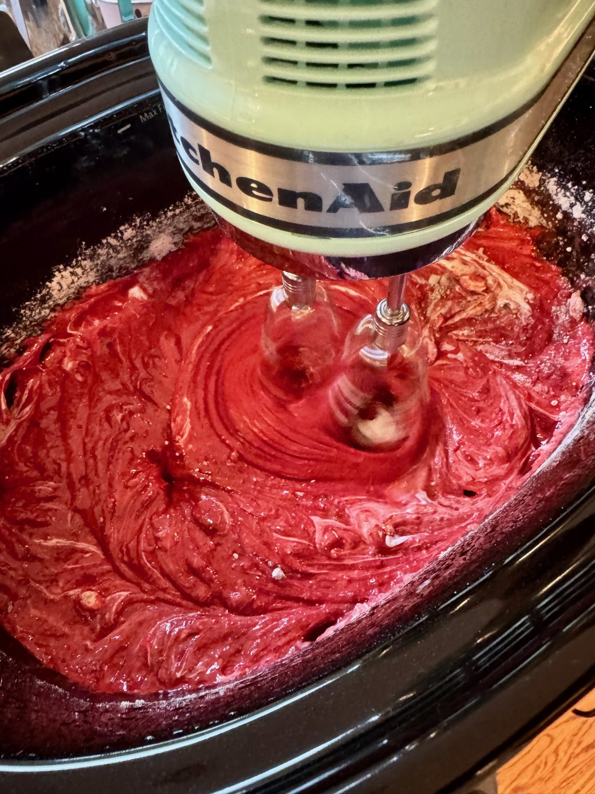 Recipe Photo for Red Velvet White Chocolate (Slow Cooker) Lava Cake. A ice blue KitchenAid Hand Mixer has finished mixing the cake mix ingredients in the black slow cooker.