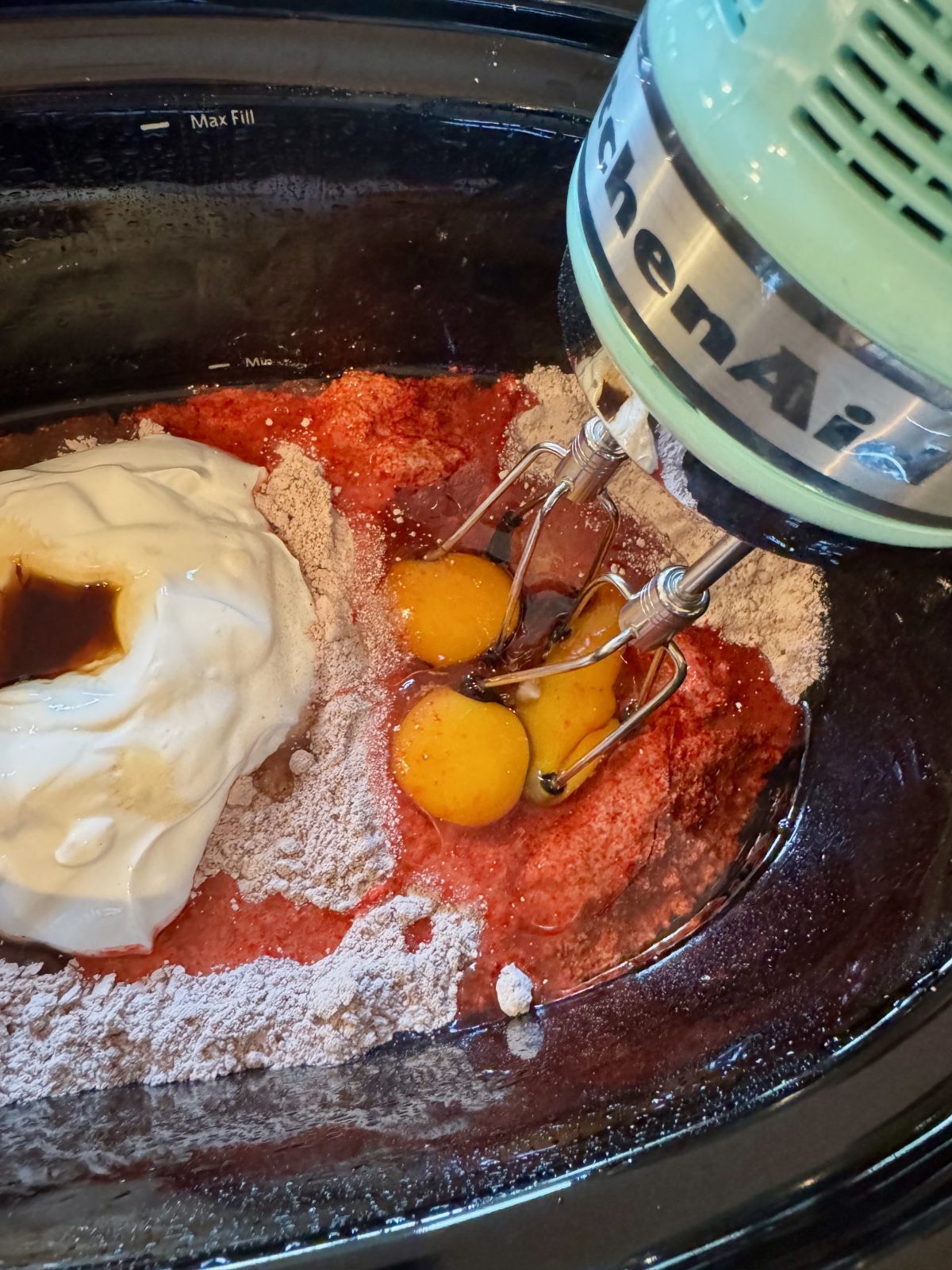 Recipe Photo for Red Velvet White Chocolate (Slow Cooker) Lava Cake. A ice blue KitchenAid Hand Mixer is starting to mix the cake mix ingredients in the black slow cooker.