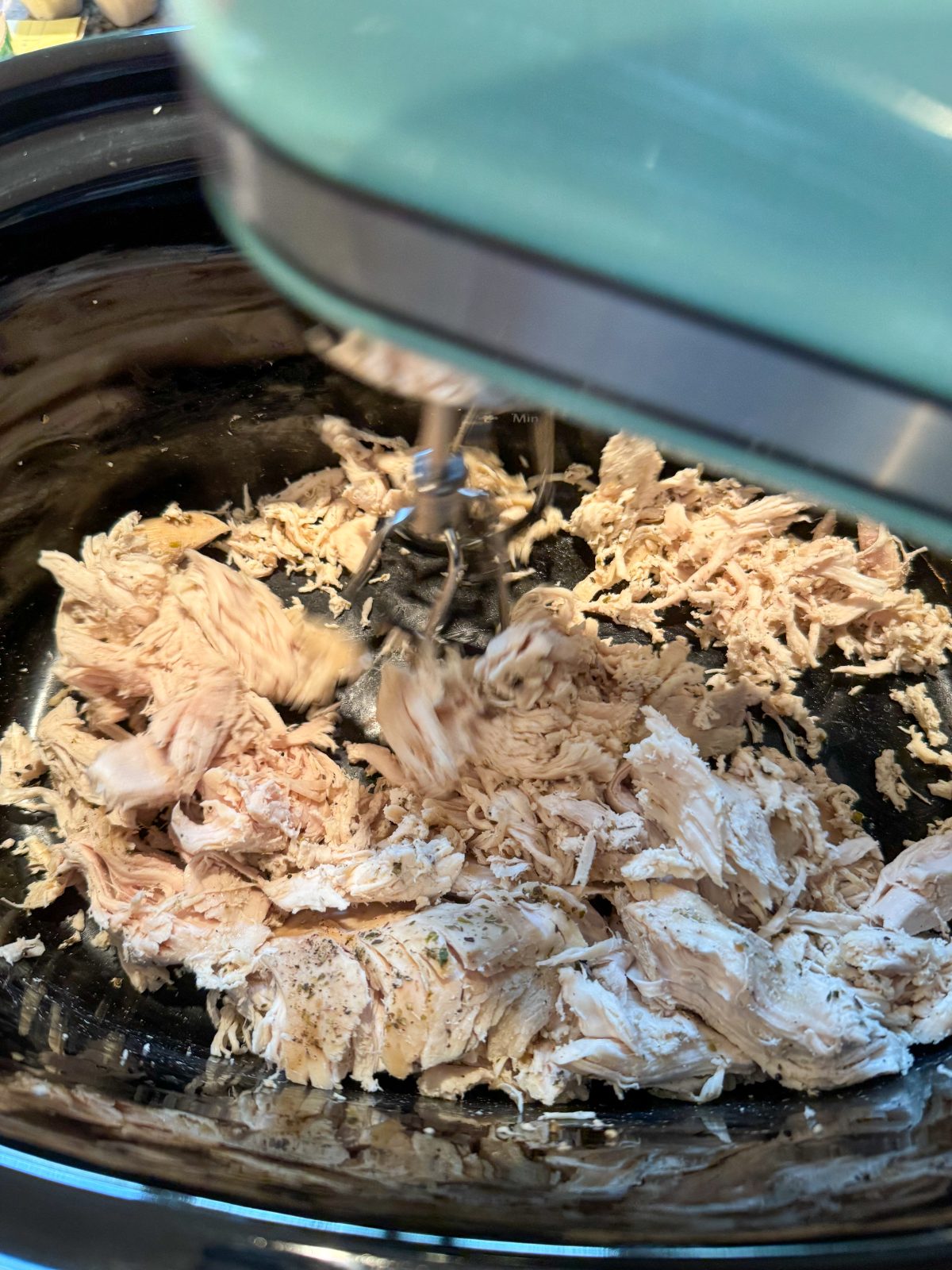 Recipe Photo for Marry Me Chicken Dip Showing a KitchenAid Hand Mixer shredding chicken breasts in a black oval slow cooker.