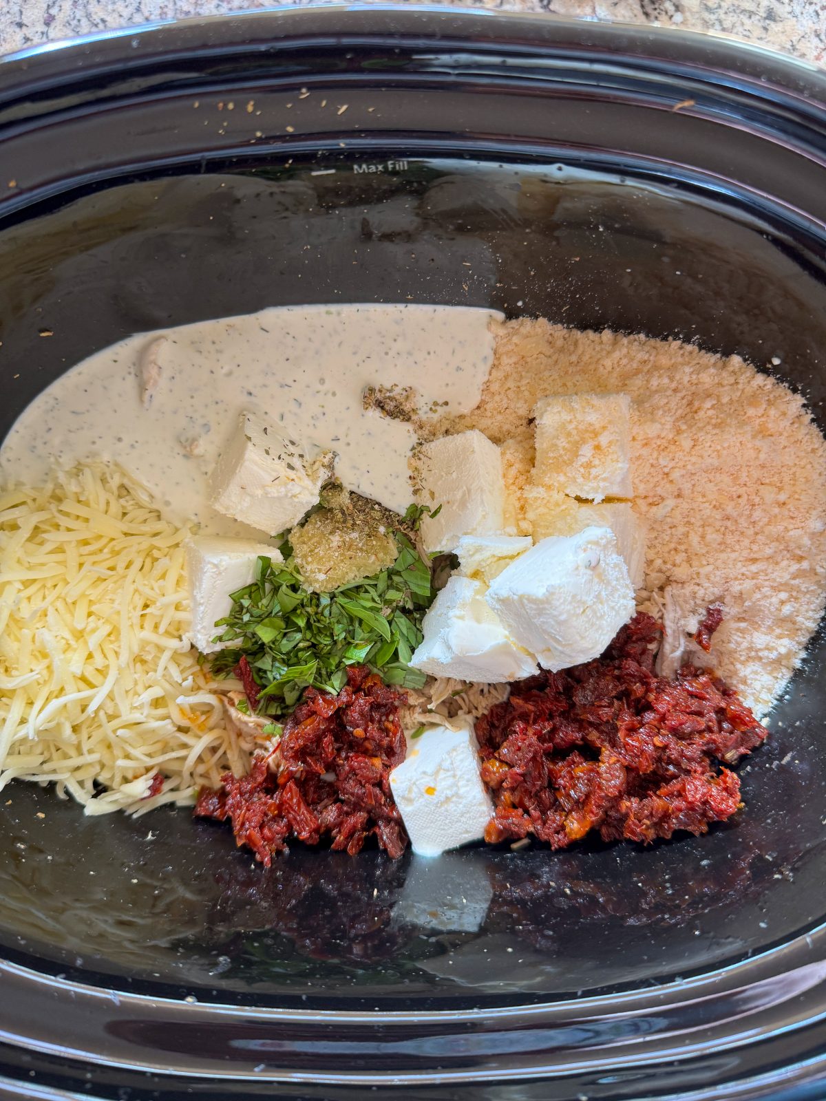 Recipe Photo for Marry Me Chicken Dip Showing all the ingredients for the dip in a black oval slow cooker. Cream cheese cubes, chopped sun dried tomatoes, Parmesan and mozzarella cheeses, ranch dressing, fresh basil and seasonings.