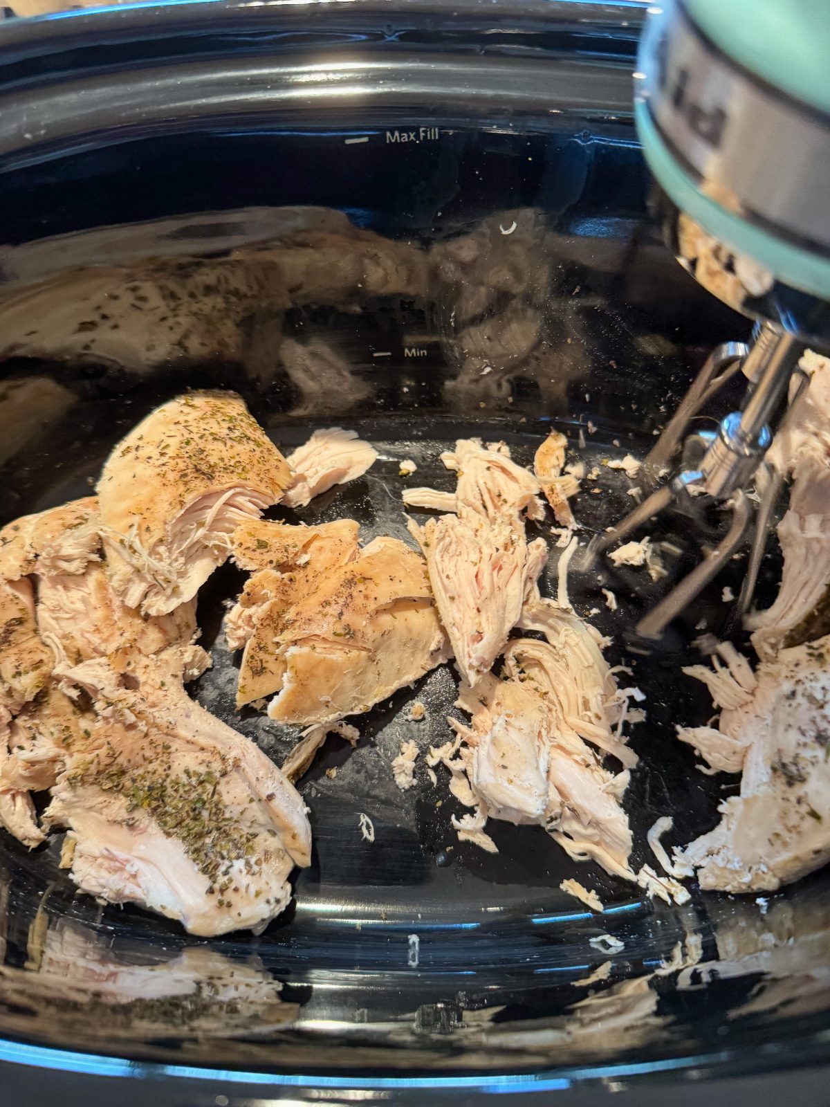 Recipe Photo for Marry Me Chicken Dip Showing a KitchenAid Hand Mixer Starting to shred chicken breasts in a black oval slow cooker.
