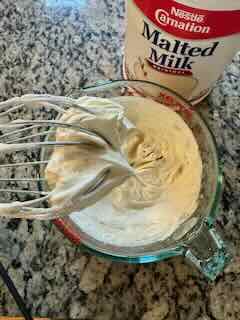 Image showing an ice blue KitchenAid 7-Speed Hand Mixer with Pro Whisk with finished Whipped Cream. A can of Carnation Malted milk powder is in the background.