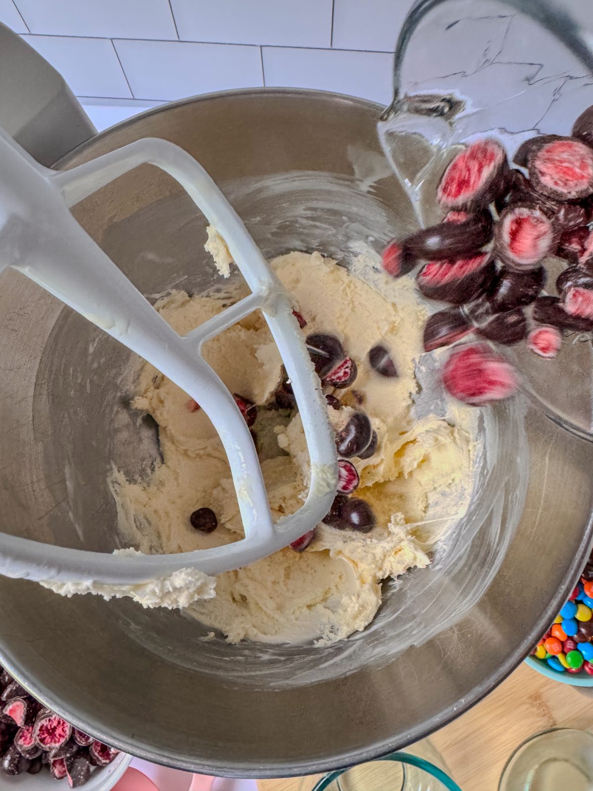 Recipe Process Photo for How to Make a Blended Blizzard Style Ice Cream Treat with Your Stand Mixer showing overhead shot of 6 scoops of vanilla ice cream inside a stainless steel KitchenAid 5qt stand mixer bowl with the white flat beater above. Crushed Tru Fru (chocolate covered dehydrated berries) candies are being poured into the bowl.
