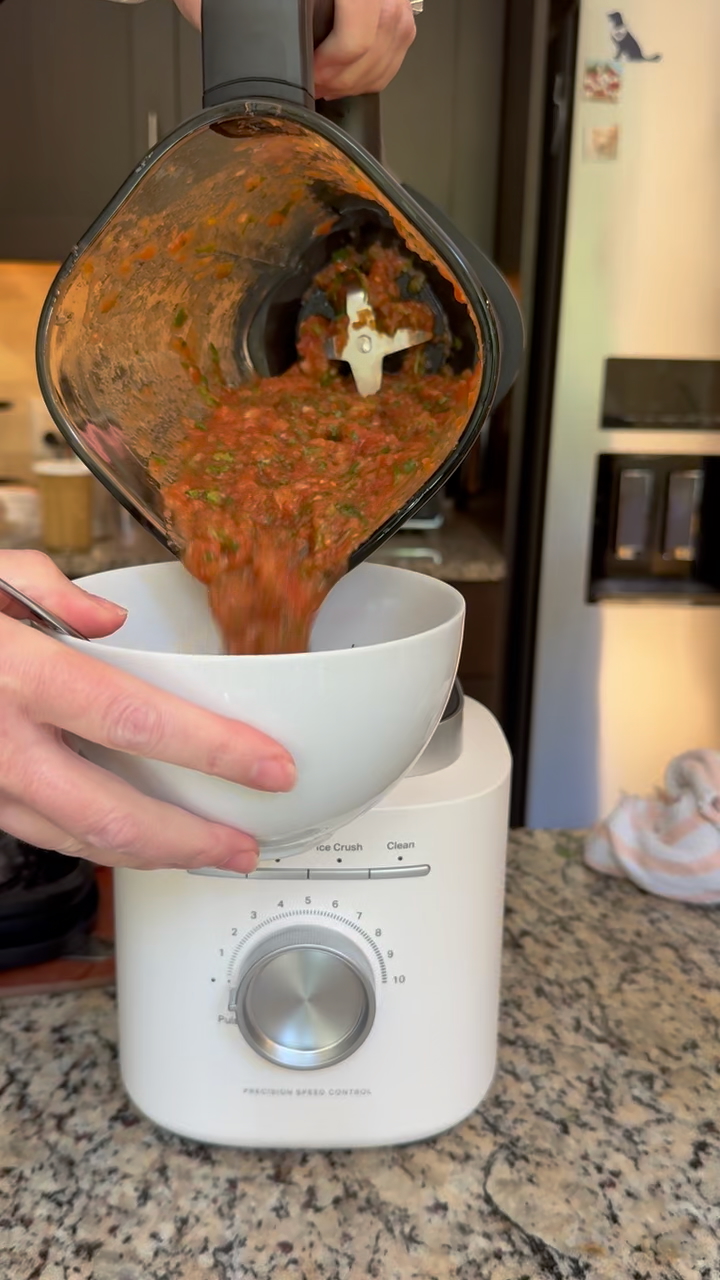 Recipe Image of Pouring out Salsa into a white bowl from the KitchenAid Pure Power Blender with glass jar. The blender is Porcelain White in color. It is sitting on a gray granite countertop and you can see a stainless steel refrigerator in the background.