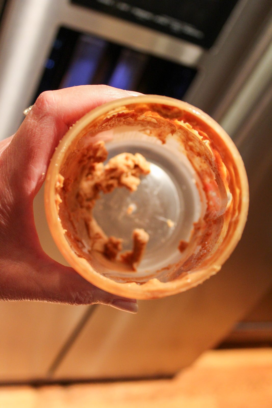 Looking inside a jar of Kirkland natural peanut butter. Jar is empty except for some dried up clumps of peanut butter.
